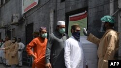 A man checks the body temperature of worshippers arriving for Friday prayers at a mosque in Lahore, Pakistan, May 1, 2020.