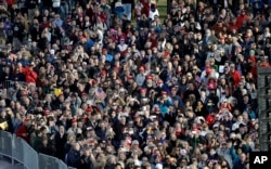 People watch video monitor showing President-elect Donald Trump laying a wreath at the Tomb of the Unknowns at Arlington National Cemetery before the start of a pre-Inaugural "Make America Great Again! Welcome Celebration" at the Lincoln Memorial in Washington, Jan. 19, 2017.