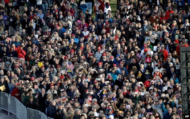 People watch video monitor showing President-elect Donald Trump laying a wreath at the Tomb of the Unknowns at Arlington National Cemetery before the start of a pre-Inaugural "Make America Great Again! Welcome Celebration" at the Lincoln Memorial in Washington, Jan. 19, 2017.