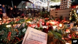 People stay in front of candles close to a Christmas market beside the Kaiser Wilhelm memorial church in Berlin, Germany, Dec. 21, 2016, two days after a truck ran into a crowded Christmas market there, killed several people and injuring dozens.