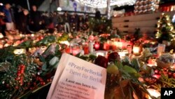 People stay in front of candles close to a Christmas market beside the Kaiser Wilhelm memorial church in Berlin, Germany, Dec. 21, 2016, two days after a truck ran into a crowded Christmas market there, killed several people and injuring dozens.