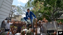 Venezuela’s National Assembly President and opposition leader Juan Guaido tries to climb the fence to enter the compound of the Assembly in Caracas, after he and other opposition lawmakers were blocked by police from entering a session to elect new Assemb