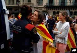 A woman wearing the Spanish and Catalonian colors greets a Catalan Mossos d'Esquadra regional police officer as people celebrate a holiday known as "Dia de la Hispanidad" or Spain's National Day in Barcelona, Oct. 12, 2017.