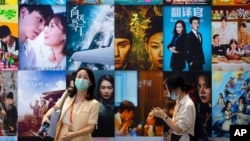 FILE - Visitors walk past a display of posters for Chinese movie and television productions at the China International Fair for Trade in Services in Beijing, Sept. 3, 2021.