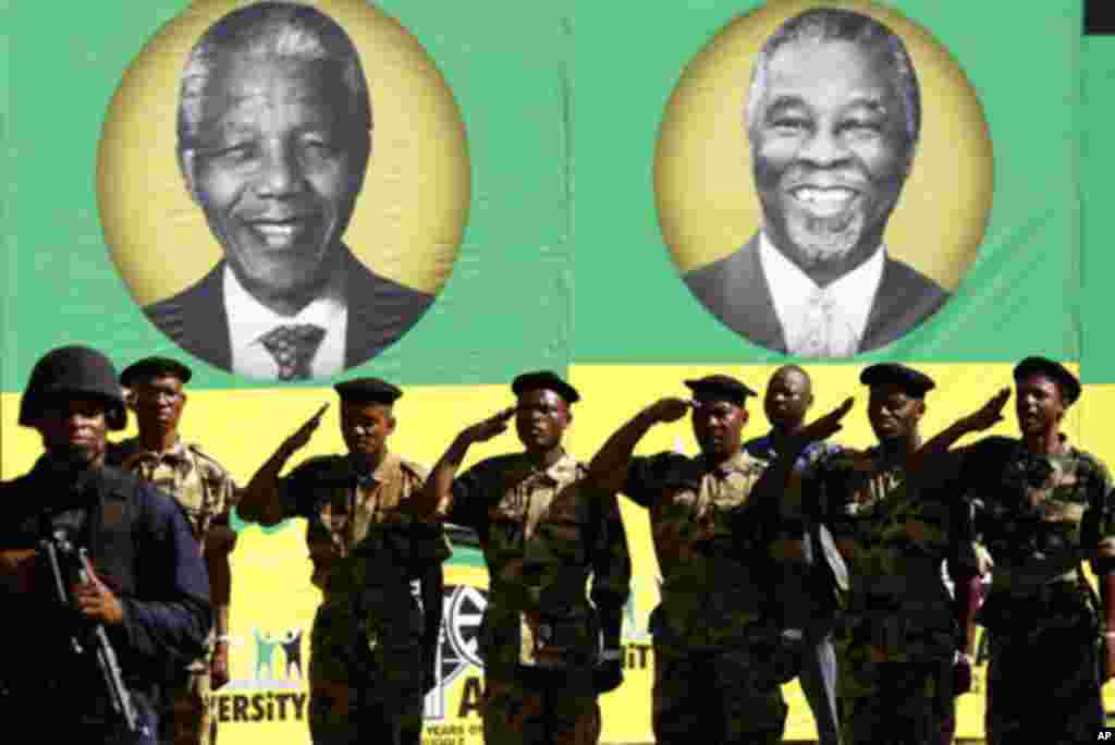 Members of the Umkhonto We Sizwe Military Veterans Association (MKMVA) salute in front of posters of former presidents of the African National Congress (ANC), Nelson Mandela (L) and Thabo Mbeki, during the ANC's centenary celebration in Bloemfontein Janua