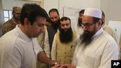 An election officer marks a thumb of Hafiz Saeed, right, head of the Pakistani religious party Jamaat-ud-Dawa, at polling station in Lahore, Pakistan, July 25, 2018. 