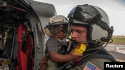 Kru Udara Angkatan Laut Brandon Larnard yang menggendong seorang pengungsi menaikin helikopter MH-60S Sea Hawk menyusul terjangan Badai Maria di pulau Dominica, 27 September 2017 on the island of Dominica, Sept. 27, 2017. 