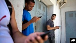 FILE - Young people gather behind a business looking for an internet signal for their smart phones in Havana, Cuba, April 1, 2014. Only 47 percent of the global population is currently connected, a new report finds.