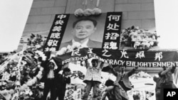 1989年4月19日中國學生在北京天安門廣場上的人民英雄紀念碑前展示胡耀邦像和“民主之光耀邦”等標語。