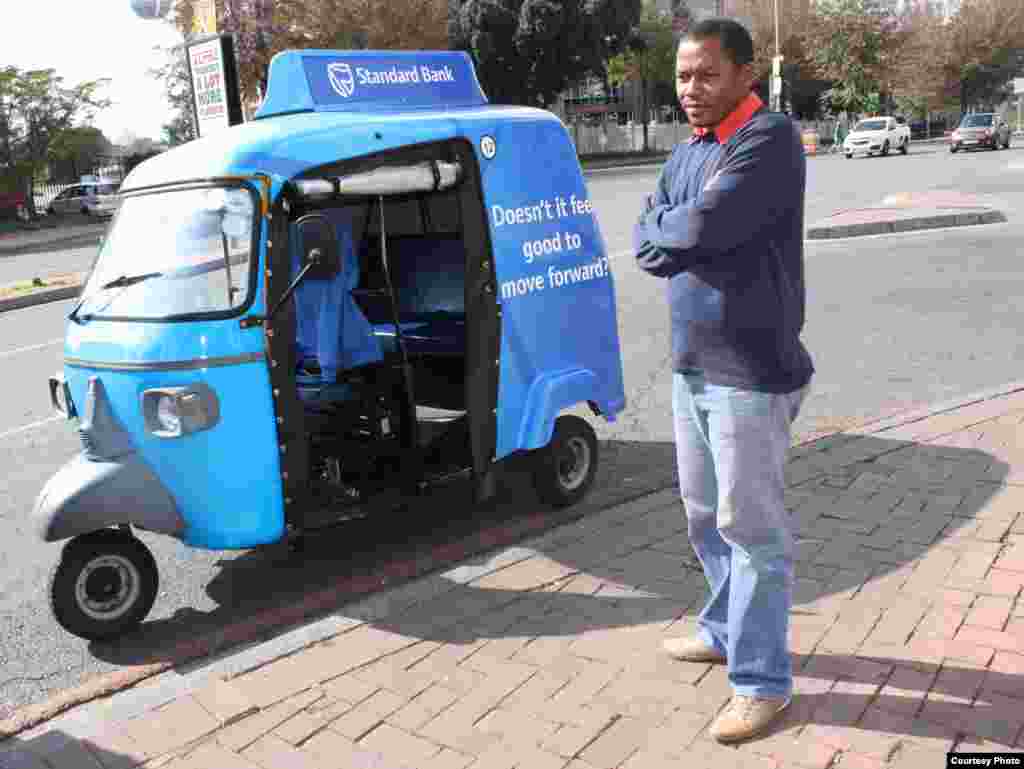 “People call our tuk tuks ‘toy cars,’” says Johannesburg driver Alan Bangi as he waits for a fare at a Sandton intersection. (Photo by Darren Taylor) 