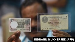 Un collectionneur tient un nouveau billet d'une roupie indienne à côté d'un billet original vieux de 100 ans, à Mumbai, le 30 novembre 2017.