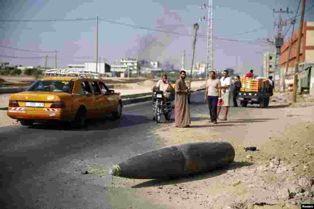 Palestinians look at an unexploded Israeli shell that landed on the main road outside the town of Deir Al-Balah, in the central Gaza Strip, August 1, 2014.