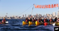 In this photo taken April 16, 2015, a group of kayakers rafted together work to pull up a protest sign as they practice for an upcoming demonstration against Arctic oil drilling, in Elliott Bay in view of downtown Seattle.