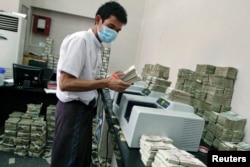 FILE - An employee counts Myanmar kyat banknotes in a bank in Yangon, April 5, 2012.