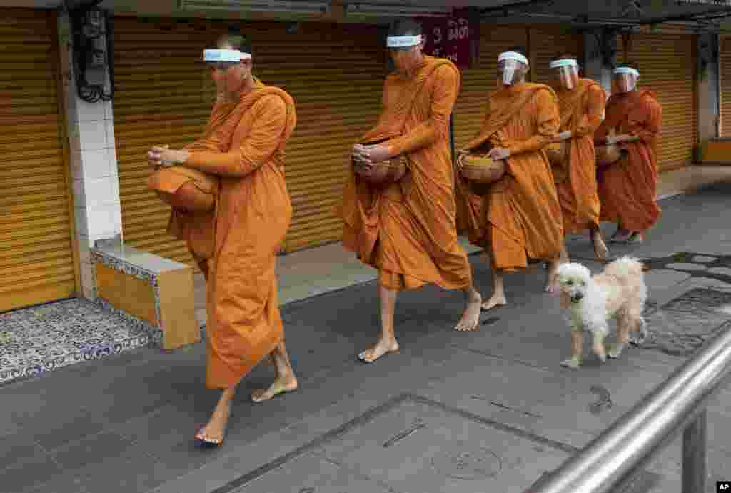 Buddhist monks with face covers to protect themselves from the new coronavirus walk to collect food donations in Bangkok, Thailand.