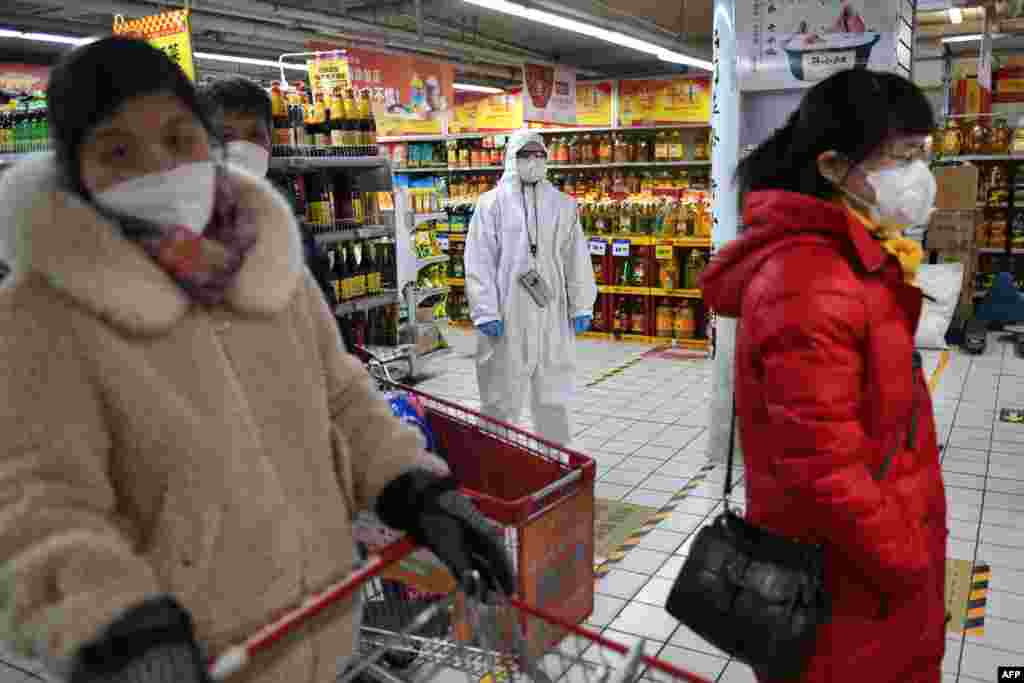 A worker wears protective clothing as a preventive measure against the COVID-19 coronavirus as she watches over customers in a supermarket in Beijing. 