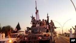 FILE - Fighters from the Islamic State group parade in a commandeered Iraqi security forces armored vehicle down a main road at the northern city of Mosul, Iraq.