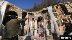 A man points out a damaged fresco in the Orthodox Church of Saint Athanasios in Leshnica, Albania, Jan. 25, 2018. 