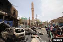 People look at the wreckage of a car at the site of a car bomb attack in Yemen's capital Sana'a, June 18, 2015.