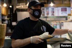 Athens Voulgaridis, owner of Olympia Gyro, serves customers at Reading Terminal Market that has seen reduced foot traffic due to the coronavirus disease (COVID-19) outbreak in Philadelphia, Pennsylvania, U.S., February 20, 2021. (REUTERS/Hannah Beier)