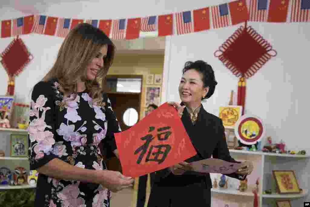 A primeira-dama da China Peng Liyuan, à direita da primeira-dama dos EUA, Melania Trump, que segura um cartaz escrito em caracteres chineses que significam &quot;Fortuna&quot;, na escola primária Banchang em Pequim, China