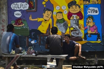 Orang-orang duduk di depan mural kampanye pemilihan umum Indonesia menjelang pemilihan bulan depan di Banda Aceh, Aceh pada 17 Maret 2019. (Foto: AFP/Chaideer Mahyuddin)