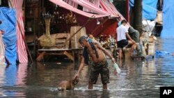 Seorang pria mengelus seekor anjing di sepanjang jalan yang tertutup banjir akibat hujang yang ditimbulkan Topan Nock-Ten (26.12). Quezon City, Utara Manila, Filipina. (foto: AP Photo/Aaron Favila)