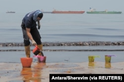 Seorang polisi menyendoki minyak yang mencemari sebuah pantai, sebagai ilustrasi. (Foto: Antara/Sheravim via REUTERS)