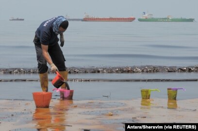 Seorang polisi menyendoki minyak yang mencemari Pantai Banua Patra dari tumpahan minyak di perairan Balikpapan, Kalimantan Timur, 2 April 2018. (Foto: Antara/Sheravim via REUTERS)