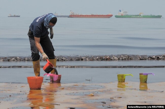 Seorang polisi menyendoki minyak yang mencemari Pantai Banua Patra dari tumpahan minyak di perairan Balikpapan, Kalimantan Timur, 2 April 2018. (Foto: Antara/Sheravim via REUTERS)