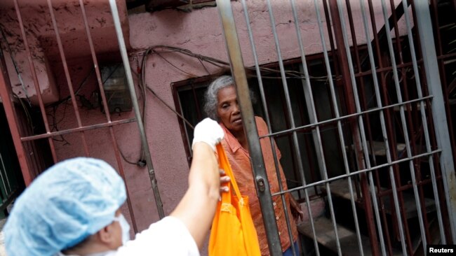 Andrea Guerrero, una anciana de 80 años, recibe una bolsa con comida en su casa de Chacao después de que el presidente en disputa de Venezuela, Nicolás Maduro, decretara una cuarentena obligatoria en todo el país.