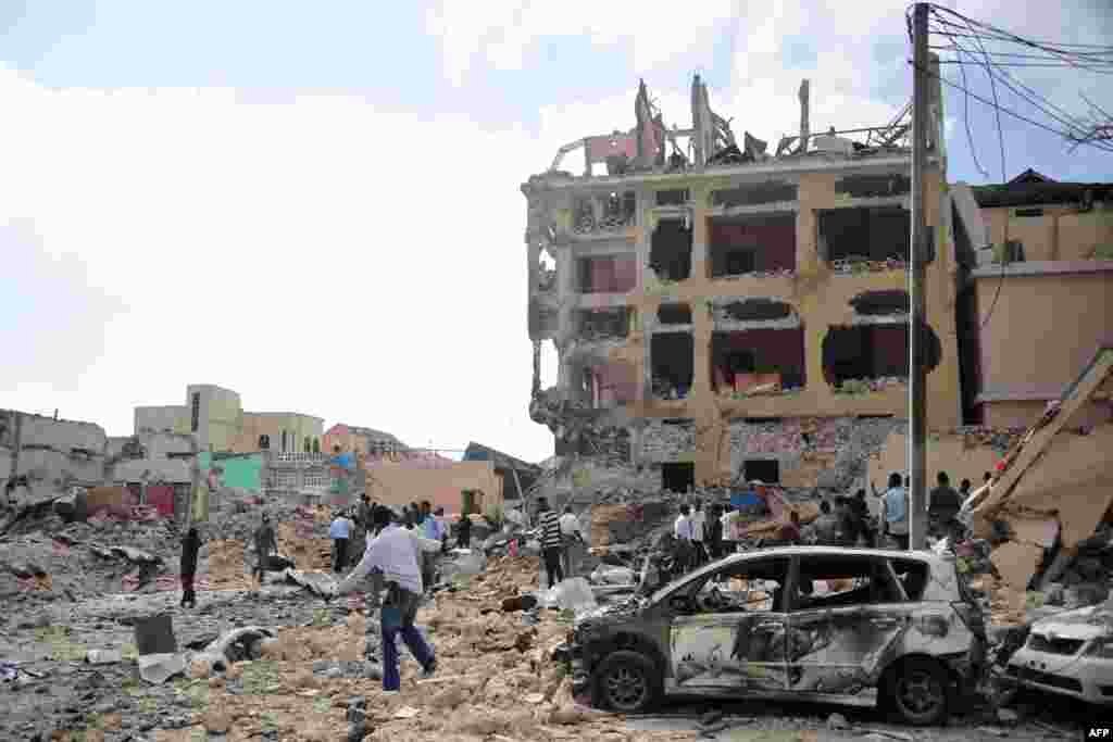 People walk in rubble following an attack outside a hotel in Mogadishu, Somalia. At least 28 people were killed after two car bombs exploded outside a popular hotel and gunmen forced their way inside the building and opened fire, police said.