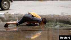 A boy is seen drinking from a puddle created by a burst water pipe in Aleppo's Karm al-Jabal district June 2, 2013.