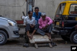 FILE - Daily wage workers check their mobile phones as they rest on a handcart at a market in Mumbai, India, Monday, Feb. 20, 2023. India’s population is expected to overtake China’s in size this year, and its economy last year surpassed that of the United Kingdom to become the world’s fifth largest. (AP Photo/Rafiq Maqbool)