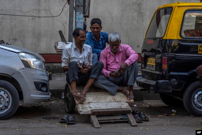 FILE - Daily wage workers check their mobile phones as they rest on a handcart at a market in Mumbai, India, Monday, Feb. 20, 2023. India’s population is expected to overtake China’s in size this year, and its economy last year surpassed that of the United Kingdom to become the world’s fifth largest. (AP Photo/Rafiq Maqbool)