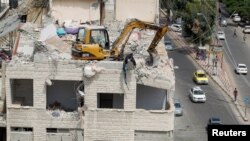 Sebuah alat berat membersihkan puing-puing dari atas atap gedung yang rusak akibat serangan udara Israel di Kota Gaza yang dikuasai Hamas di wilayah Palestina, Minggu, 25 Juli 2021. 