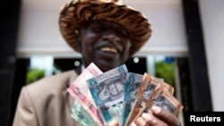 FILE- A man from South Sudan displays new currency notes outside the Central Bank of South Sudan in Juba, July 18, 2011.