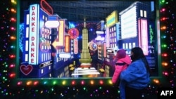 A woman holds up her to child to view holiday decorations of a window display at Macy's Herald Square store on November 24, 2020 in New York City