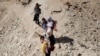 (FILE) Women carry their children while crossing from Lebanon into Syria on foot at the Masnaa border crossing, October 14, 2024.