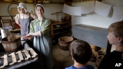 FILE - Hannah Ingersoll (L) and Loralei Arndt (2nd-L) reenact 1830s farm workers as children look on in a cheese room at Old Sturbridge Village, in Sturbridge, Mass., Aug. 22, 2018. 