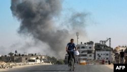 A man cycles as behind smoke from Israeli bombardment rises in an area that was ordered to be evacuated by the Israeli army in the southeast of Khan Yunis in the southern Gaza Strip, Sept. 8, 2024.