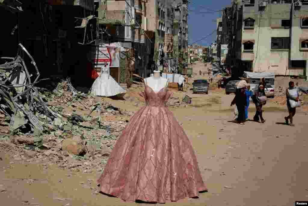 Wedding dresses for sale are displayed on mannequins outside a damaged shop as displaced Palestinians make their way to flee the area following an Israeli evacuation order in Khan Younis in the southern Gaza Strip, Oct. 7, 2024, amid the ongoing conflict between Israel and Hamas.