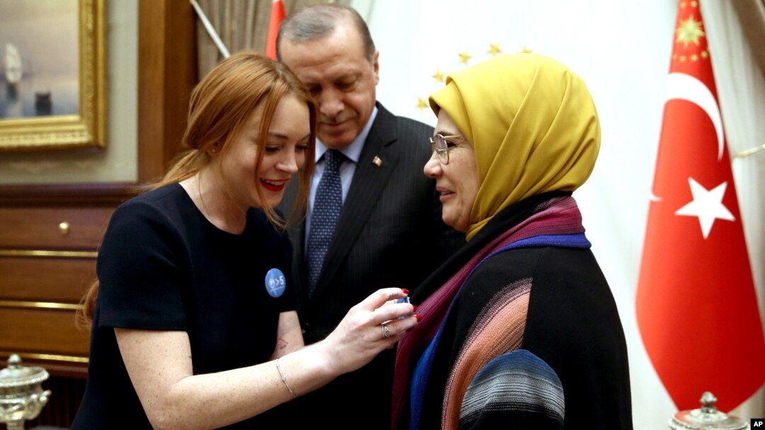 FILE - U.S. actress Lindsay Lohan, left, places a badge bearing a quote from Turkey's President Recep Tayyip Erdogan, center, reading "World is bigger than five," referring to the UN Security Council's five permanent members.