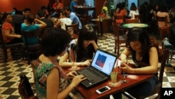 FILE - Three young Vietnamese girls use a laptop and smart phones to go online at a cafe in Ha Noi, Vietnam, May 14, 2013. 