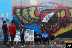 In this Sunday, Nov. 17, 2019 photo, protesters read donated books in front of graffiti, at the Saadoun Tunnel, in Baghdad, Iraq. The tunnel that passes under Baghdad’s landmark Tahrir Square has become an ad hoc museum for Iraq's revolution: Young artist