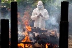 Seorang kerabat menggunakan APD melakukan ritual di dekat tubuh seseorang yang meninggal karena COVID-19 saat dikremasi di Gauhati, India, Senin, 24 Mei 2021. (Foto: AP)