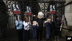 Protester wears a Rupert Murdoch mask, holds puppets of British PM David Cameron, left, and Culture Secretary Jeremy Hunt, outside Lord Justice Brian Leveson's inquiry, High Court, London, April 25, 2012.