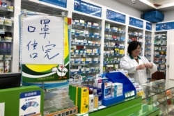 Pharmacist Liu Zhuzhen stands near a sign reading "face masks are sold out" at her pharmacy in Shanghai, Jan. 21, 2020.