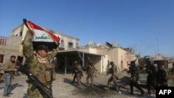 A member of the Iraqi security forces holds an Iraqi flag near the Anbar province police headquarters building in Ramadi, Iraq, Dec. 28, 2015.