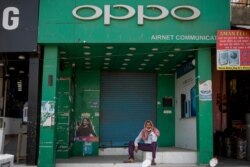 FILE - An Indian man speaks on his mobile phone in front of a shop selling OPPO phones, a Chinese consumer electronics company, in Noida, outskirts of New Delhi, India, June 18, 2020.